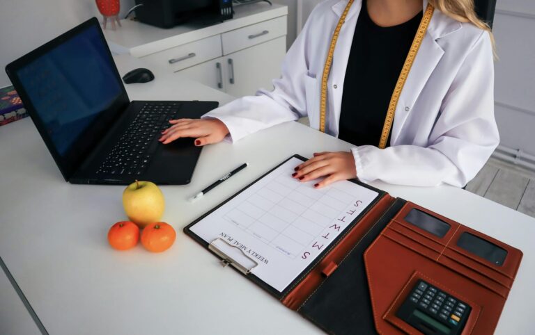 Dietitian working on meal plan with laptop, fruits, and calendar for health consultation.